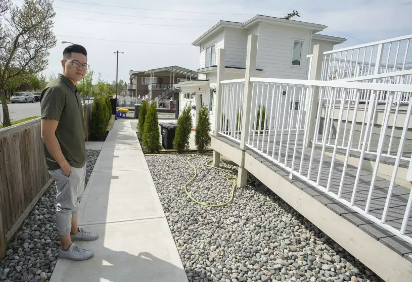 Photo of young man standing Infront of white Lane way house with white metal railings.