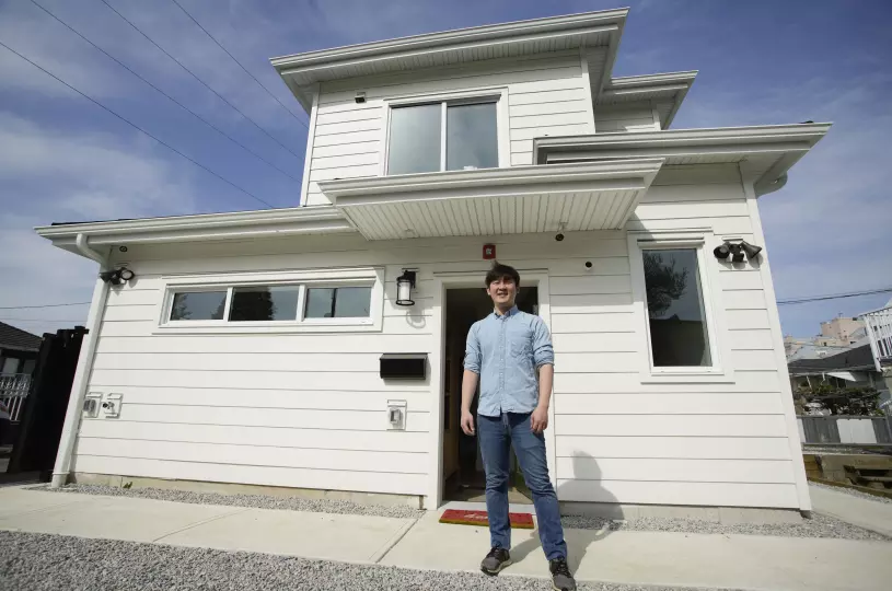 Photo of young man standing Infront of white Laneway house.