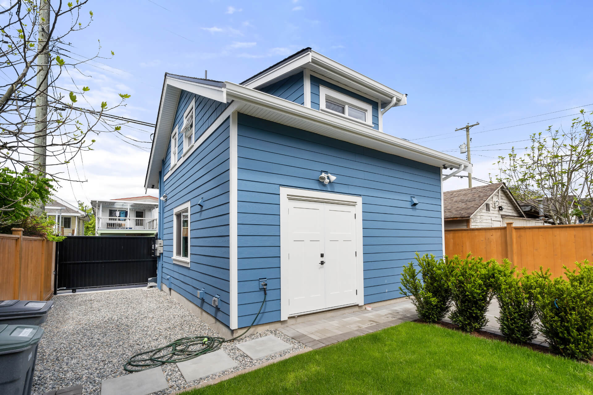 Photo of backside of blue sided Lane way house with white trim, lawn and bushes.