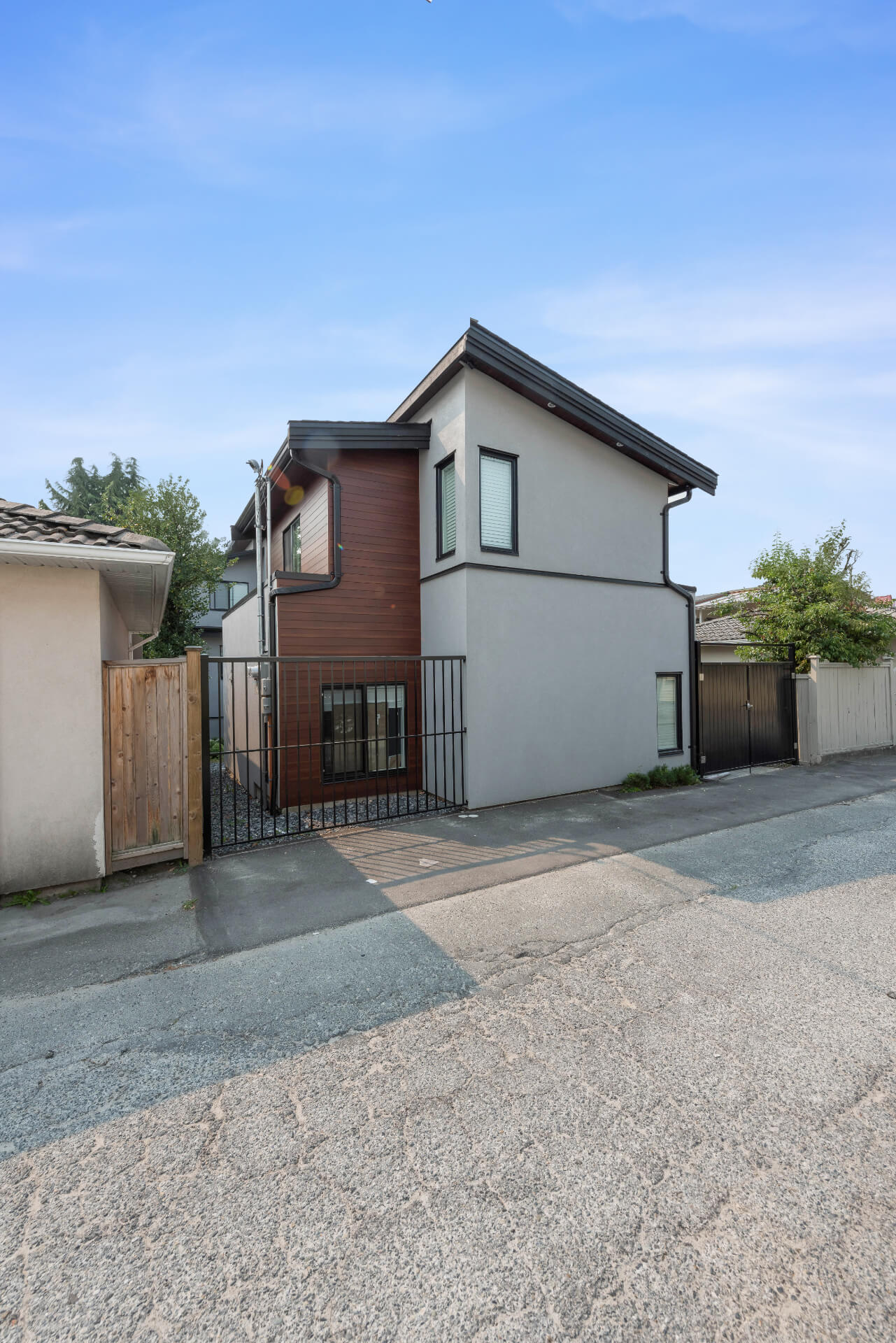 Sideview photo of Lane way house with grey stucco and brown siding.